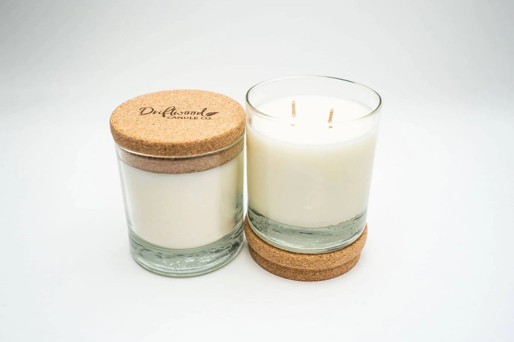 Two soy candles on a white backdrop.  First candle has a cork lid stamped with the Driftwood Candle Co. logo second is a double wick candle sitting on top of its cork lid.