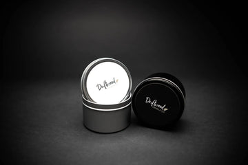 Two Travel Tins on a black backdrop.  First tin on the left is silver with lid balancing on it's side, second tin is black and is resting on its side next to the silver tin.