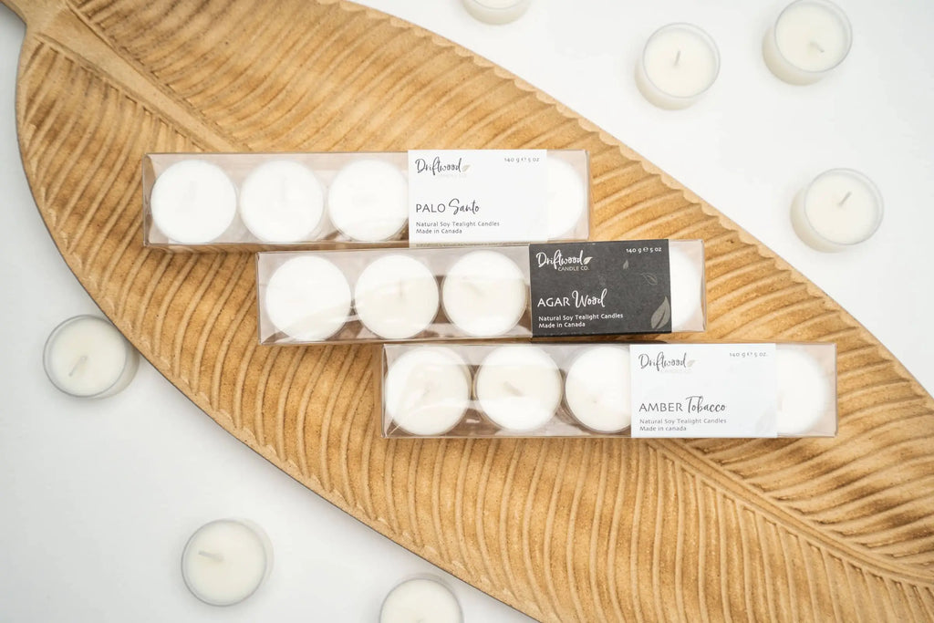 Overhead shot of three sets of Driftwood Candle co. scented tealight displayed on a wooden leaf tray with scattered tealights surrounding them.