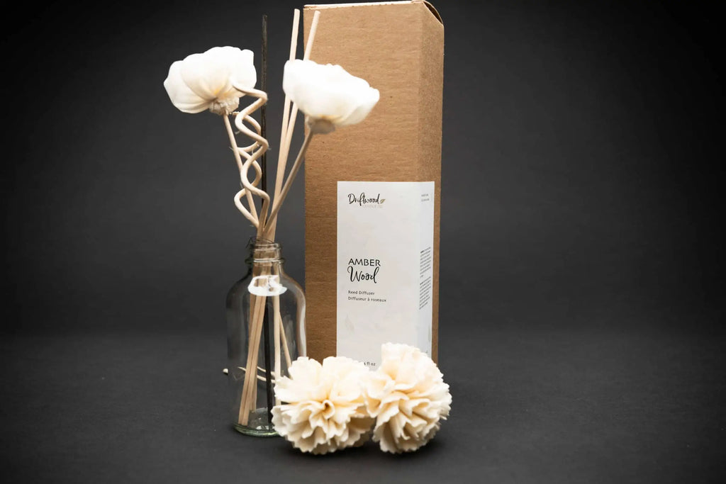 Amber Wood Reed Diffuser Set on a black backdrop.  Display includes the home fragrance oil, two sola flowers and reed diffuser sticks.  Driftwood Candle Co. scent label is on a kraft box.