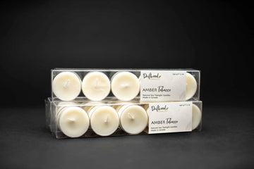 Two clear vinyl boxes filled with ten Amber Tobacco tealights.  Driftwood Candle Co. scent label affixed to the packaging.  Display is on a black backdrop for a moody effect.