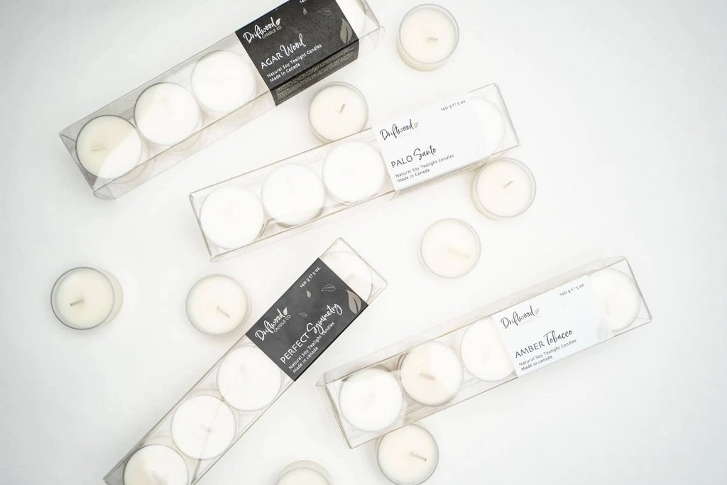 Overhead shot of four clear tealight boxes filled with ten scented tealights in each box.  Loose tealights adorn the boxes for a lifestyle shot.