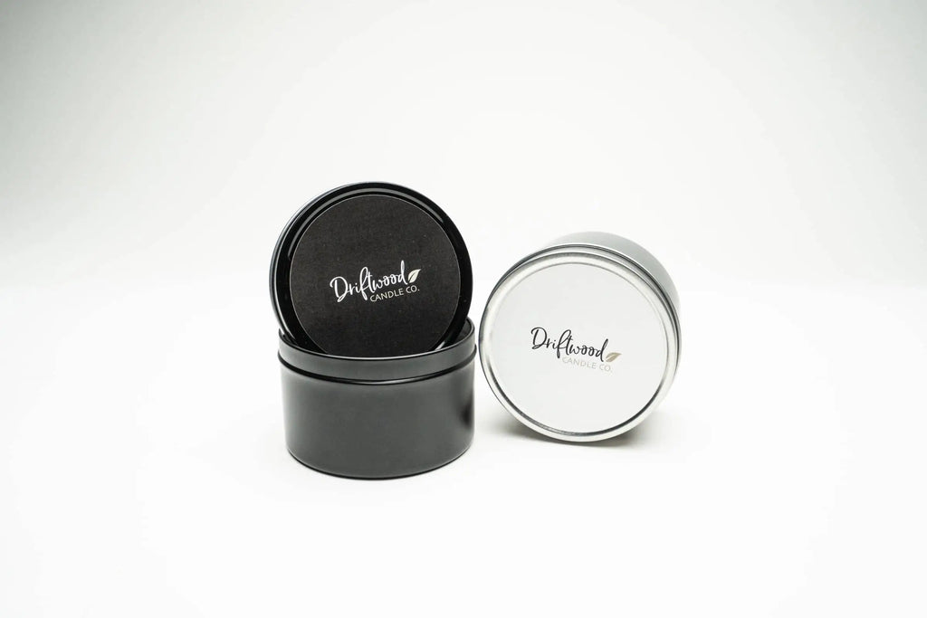 Two soy travel tins on a white backdrop.  One tin is black with a black label the other is silver with a white label.