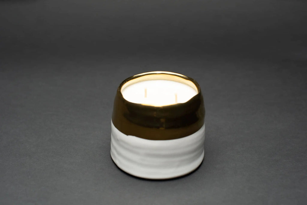 Double wicked soy candle displayed on a black backdrop.  Ceramic jar has a large white bottom band and the top band is gold rimmed.